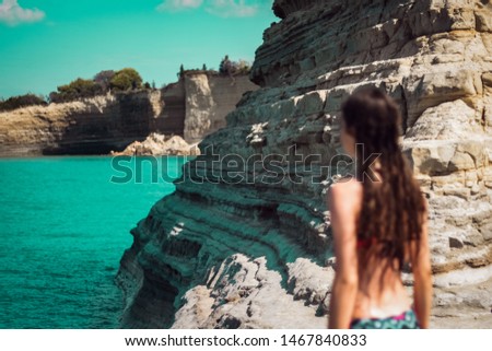 Image of a girl intentionally blurred on a cliff surrounded by sea. Girl looking in front admiring the view in Corfu island, Greece.