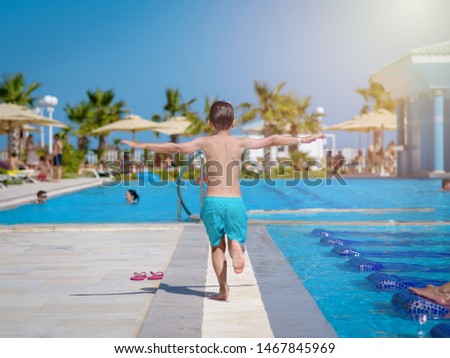 Caucasian boy running along swimming pool at resort. He is moving away from camera.