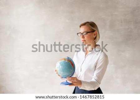 Young teacher posing with globe in hands on background of empty wall