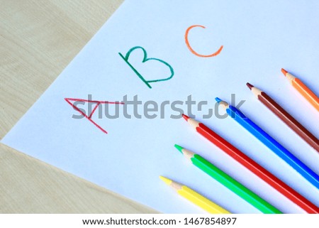 Back to school concept. Six multicolored pencils on a white sheet of paper with letters 'A', 'B', 'C'. Selective focus.