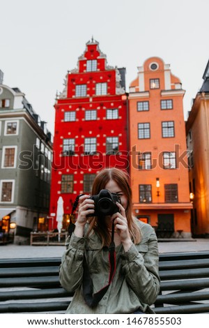 Hipster hiker tourist taking photo on camera on background of atmospheric city with beautiful colorful houses of Stockholm, photographer woman enjoying light of holiday