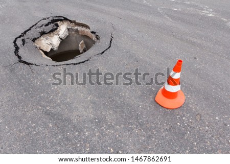Large hole on asphalt road surface and orange traffic cones. Accident hazard. Pit on the street city. Damaged pavement surface.