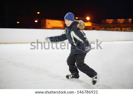 Happy boy wearing in black suit skates at dark winter night.