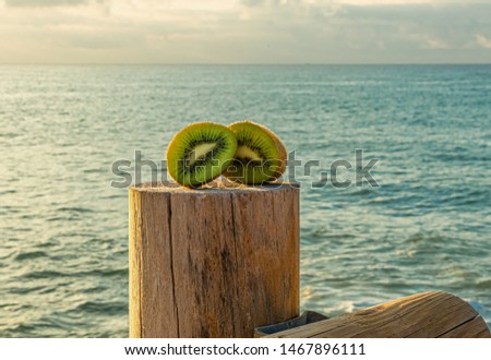 A green and fresh green kiwi cut in half on a rustic wooden dock with sea on the background - Freshly harvested kiwi - Blue water