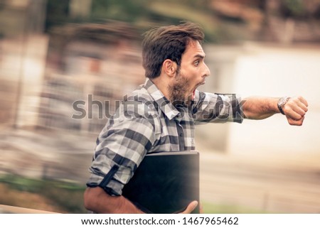 Stressed and anxious young man in a hurry, checking time and running, being late, holding his laptop in one hand Royalty-Free Stock Photo #1467965462