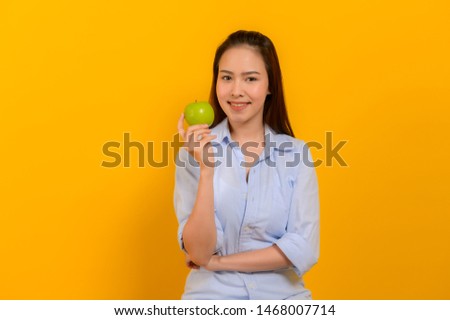 Healthy  or dieting concept : Portrait photo of young beautiful Asian woman holding green apple and smiling on yellow background.