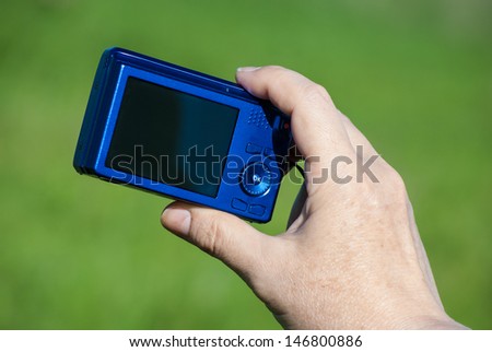 woman's hand with compact digital photo camera against green background