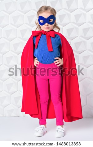 A full length portrait of a funny child girl wearing a costume of a hero and posing in the studio over the white background. Kids, fashion, costume, hero.
