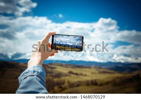 Close-up of female hand holding smartphone and taking photo or video. Woman traveler on the background of a snowy mountain range takes photos on a mobile phone. The concept of travel.