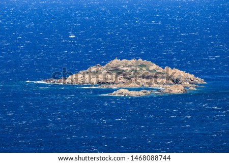 View from above, stunning aerial view of a rough sea with a small rocky island and a sailboat in the background. Sardinia, Italy.
