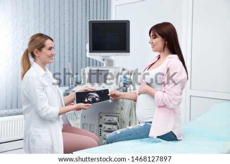 Doctor showing ultrasound image of baby to future mother in clinic
