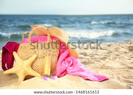 Bag with starfish, swimsuit, hat, sunglasses and cosmetics on sand beach