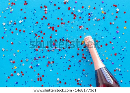 Champagne bottle with colorful party streamers for celebration on blue background top view pattern
