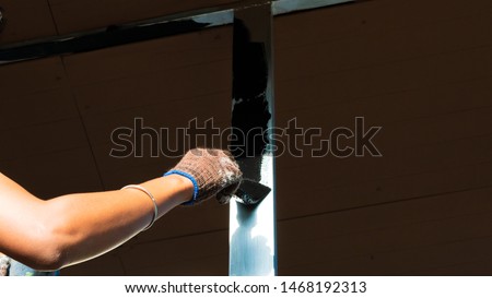 The concept of rustproof painting on steel structures. The Hand holding paintbrush is painted black on the surface of the steel. Selected focus.