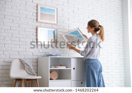 Decorator hanging picture on white brick wall in room. Interior design Royalty-Free Stock Photo #1468202264