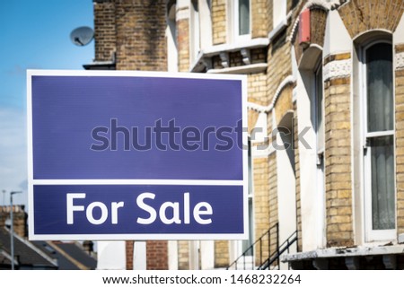 Estate agent 'For Sale' sign with houses in background