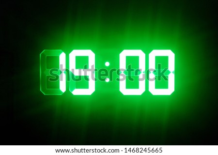 Green glowing digital clocks in the dark show 19:00 time