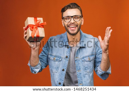 Happy holidays! Adorable photo of attractive man with beautiful smile with present box isolated over orange wall. 