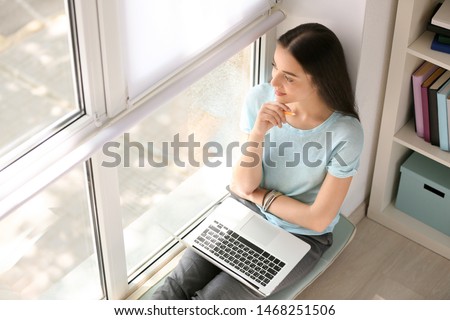 Female student with laptop preparing for exam near window