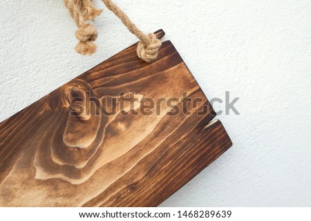 Wooden rustic crunched plate hanging with ropes with empty space for writing. Hollidays or sale or winter or new year concept. Brown wooden vintage signboard hanging against the white wall.