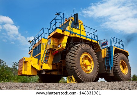 A picture of a big yellow mining truck at work site on blue sky with white clouds background