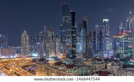 Aerial view of illuminated skyscrapers and road junction in Dubai night timelapse. Traffic on intersection in downtown with modern towers around. Cloudy sky