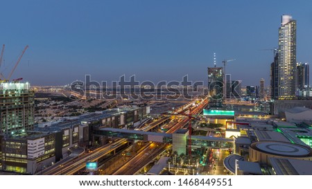Aerial view of Financial center road day to night transition timelapse with shopping mall and under construction building with cranes from downtown, Dubai Creek harbor on background