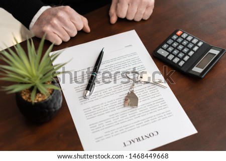 Hands of customer in front of real estate contract with house keys before signing