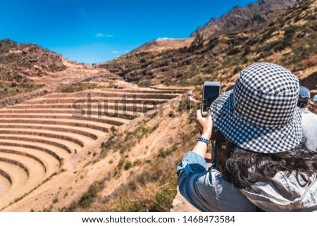 A tourist woman taking a picture of the ruins of Pisac with her smartphone in the Sacred Valley of the Incas. Cusco region, Peru.