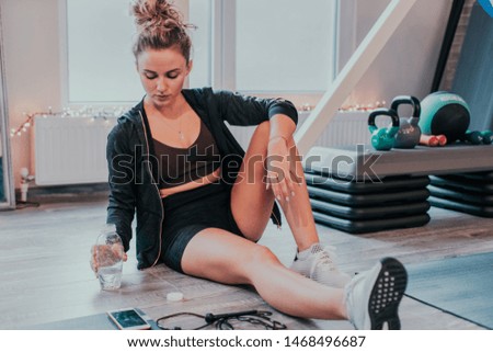 Pretty lady after she finished her workout in a large spacious equipped studio have a relaxed time feeling tired and thirsty drinking some water