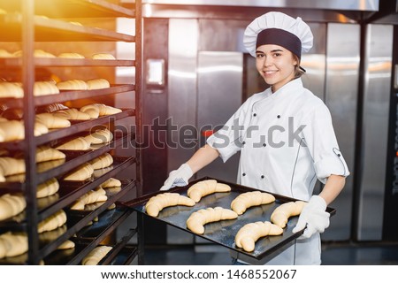Baker girl with a baking sheet with raw dough in hands on the background of an industrial oven in a bakery Royalty-Free Stock Photo #1468552067