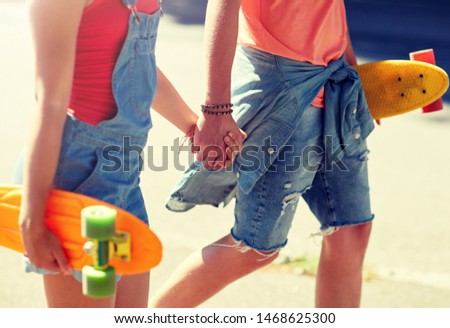 summer, relations, extreme sport and people concept - close up of happy teenage couple with short modern cruiser skateboards walking along city street