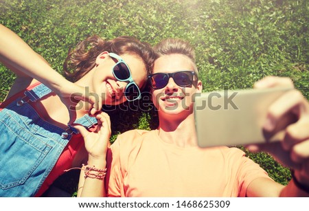 love and people concept - happy teenage couple in sunglasses lying on grass and taking selfie on smartphone at summer