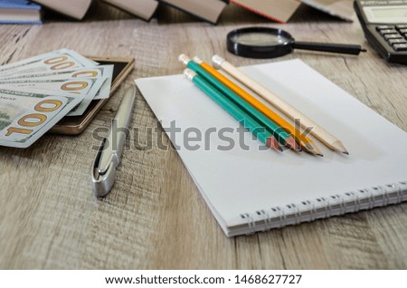 Notepad with books and pencils on the table. Dollars, calculator and smartphone. Office concept.