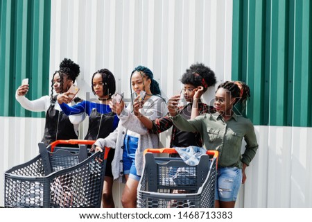 Group of five african american woman with shopping carts making selfie on mobile phone outdoor.