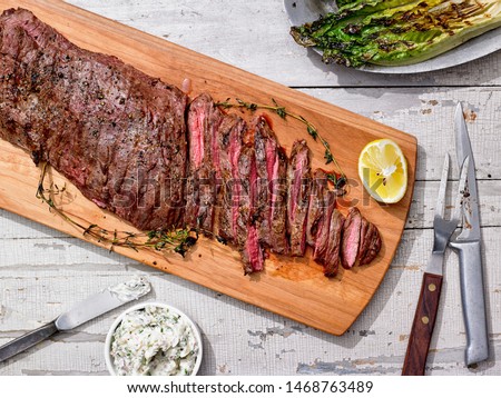 Grilled Skirt Steak sliced with Shallot Thyme Butter and asparagus on cutting board with fork and knife Royalty-Free Stock Photo #1468763489
