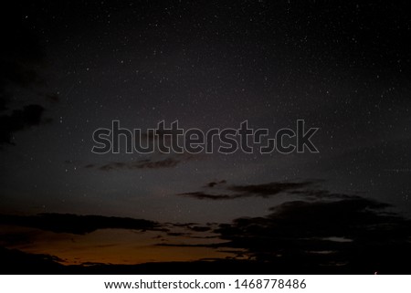 Beautiful summer night sky filled with stars and clouds, orange in the background from the sun setting