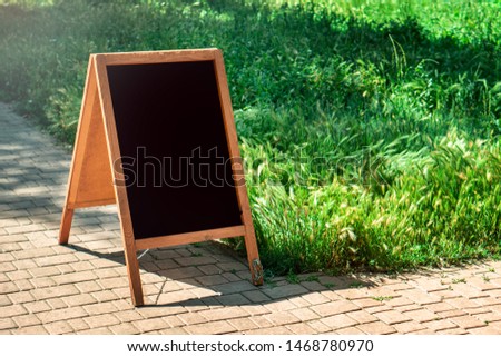 A black chalkboard stand on wood for a restaurant menu in the street. Empty menu board on street. Empty menu board on street on the pub or restaurant background. Beauty and minimalism style