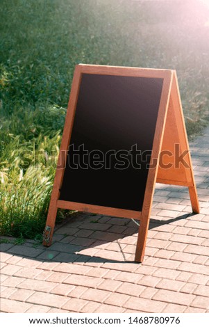 A black chalkboard stand on wood for a restaurant menu in the street. Empty menu board on street. Empty menu board on street on the pub or restaurant background. Beauty and minimalism style