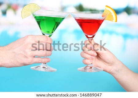 Cocktails in men's and women's hands on pool background