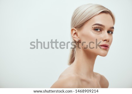 Perfection. Beautiful and young blonde woman with black surgical lines on eyelids and under eyes looking at camera Royalty-Free Stock Photo #1468909214