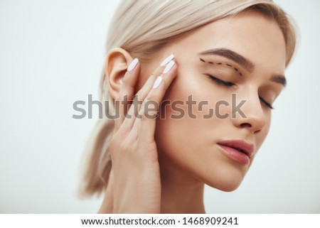Plastic surgery. Beautiful young blonde woman keeping eyes closed and touching her face with sketch on it Royalty-Free Stock Photo #1468909241