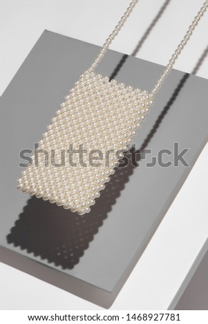 Object picture of crossbody pearls phone bag. The photo is taken on grey and white background. The bag is casting shadow on grey part of background. 