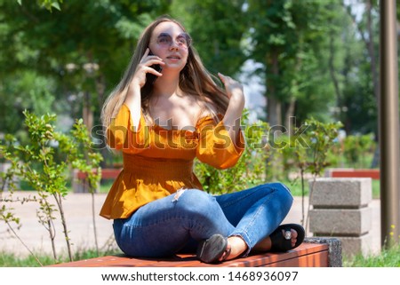 Close-up portrait of glamorous girl in glasses talking on phone. Outdoor portrait a blonde young woman talking by her smartphone and smiles.