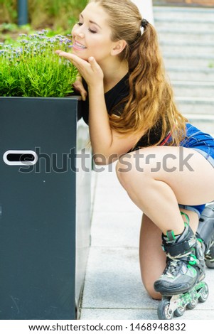 Happy joyful young woman wearing roller skates riding in town smelling flowers. Female being sporty having fun during summer time.