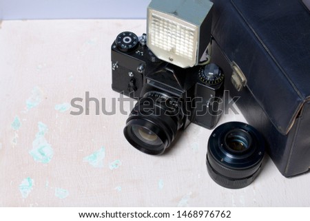 Old film camera, removable lens and wired flash. They lie on the surface of the table.
