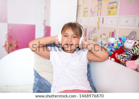 Close up portrait of little caucasian adorable girl listening to music in earphones in cozy bedroom smiling and relaxing. Happiness, leisure, children lifestyle, childhood, gadget,technology concept