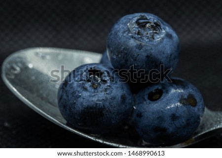 Blueberries Macro close-up photo of stacked and side by side in a teaspoon on a dark background covered with small drops of water.