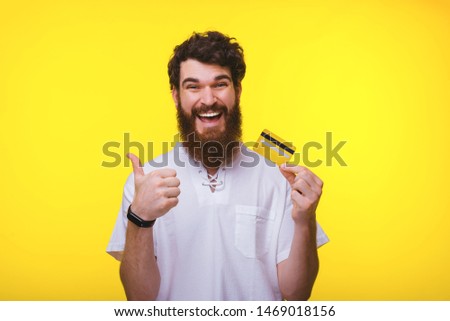 Photo of smiling bearded man showing thumbs up and holding yellow credit card, best card for online shopping