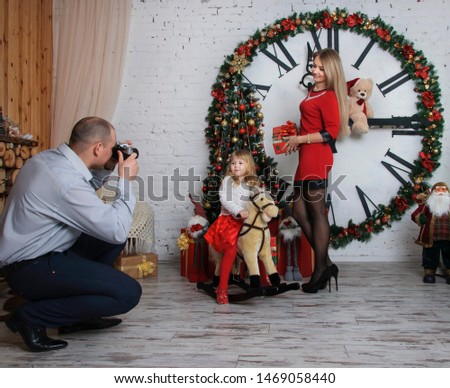New Year's shooting of a happy family. Dad takes pictures of his wife and daughter. Girl sitting on a toy horse.